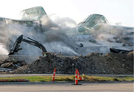 Image shows a building in the background partially demolished, with scrap material and machinery in the foreground supporting the project. 