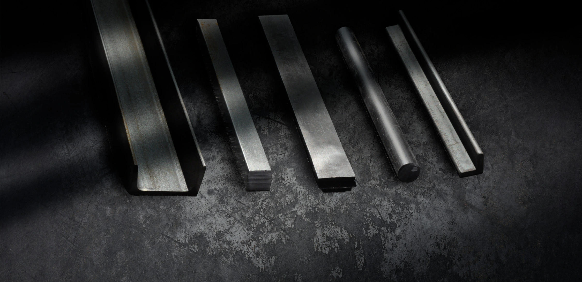A collection of metal products, including channels, squares, flats and rounds, on a dark somewhat gritty background.
