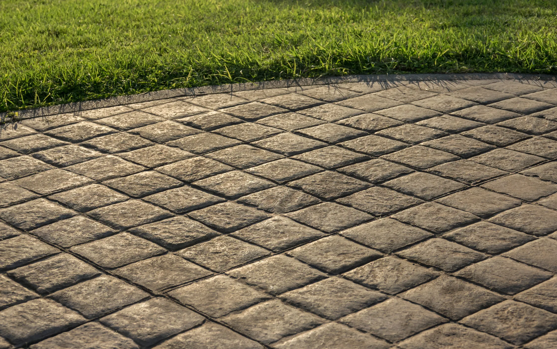An outdoors image of concrete floor that's been stamped into a grid pattern, with visible grass above.
